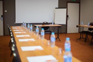 Un salón de conferencias con una larga mesa, sillas, botellas de agua y una pizarra.