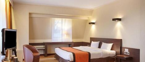 A hotel room with a large bed, a desk, a chair, and a television.