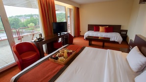 Ein Hotelzimmer mit einem Bett, einem Schreibtisch mit Fernseher, einem Sessel und einem Balkon mit Geländer.