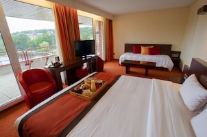 Habitación de hotel con cama, escritorio con televisor, una silla y balcón con barandilla.
