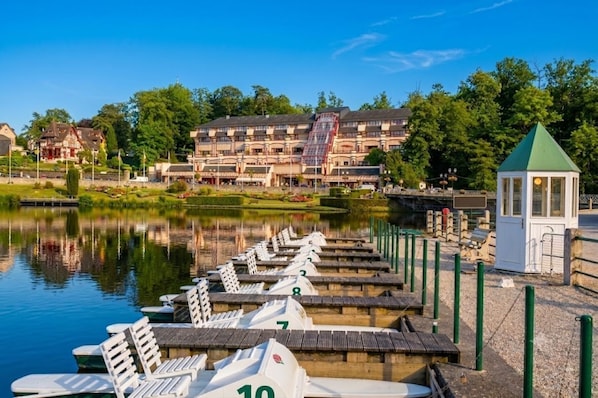 Une jetée au bord du lac avec des bateaux numérotés, un petit kiosque et une rangée de bâtiments en arrière-plan.