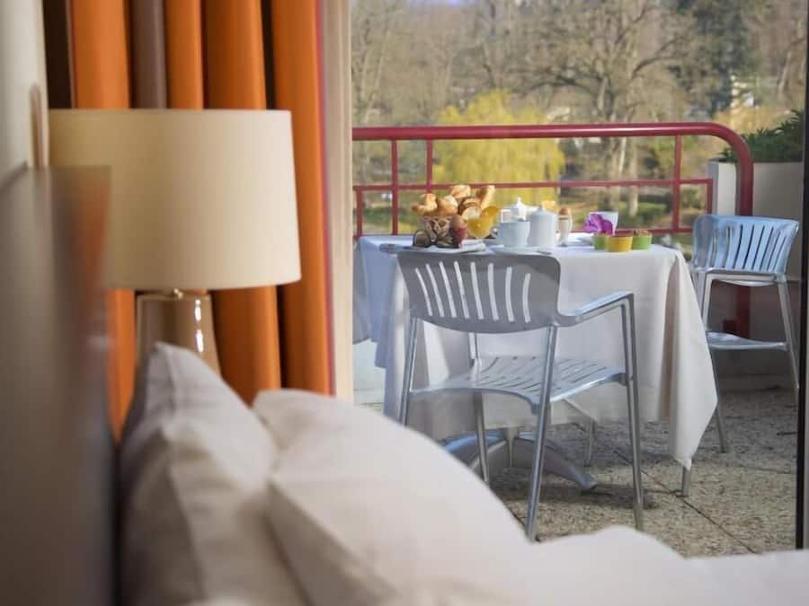 A balcony with a table set for breakfast, a chair, and a view of trees and buildings.