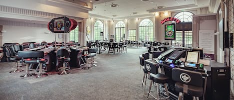 A large room with multiple gaming tables and chairs, a roulette wheel, and a sign indicating a roulette game.