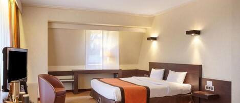 A hotel room with a bed, a desk, a chair, a television, and a window.