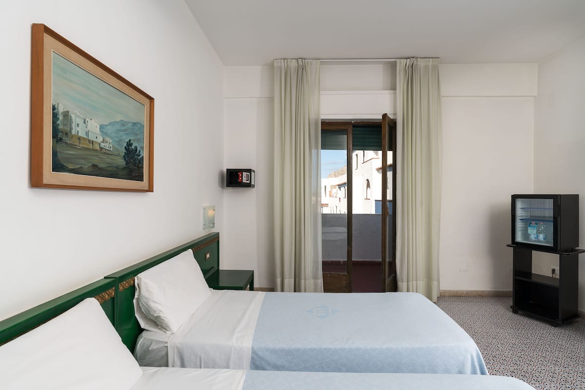 A hotel room with a bed, a painting, a television, and a view through a door.