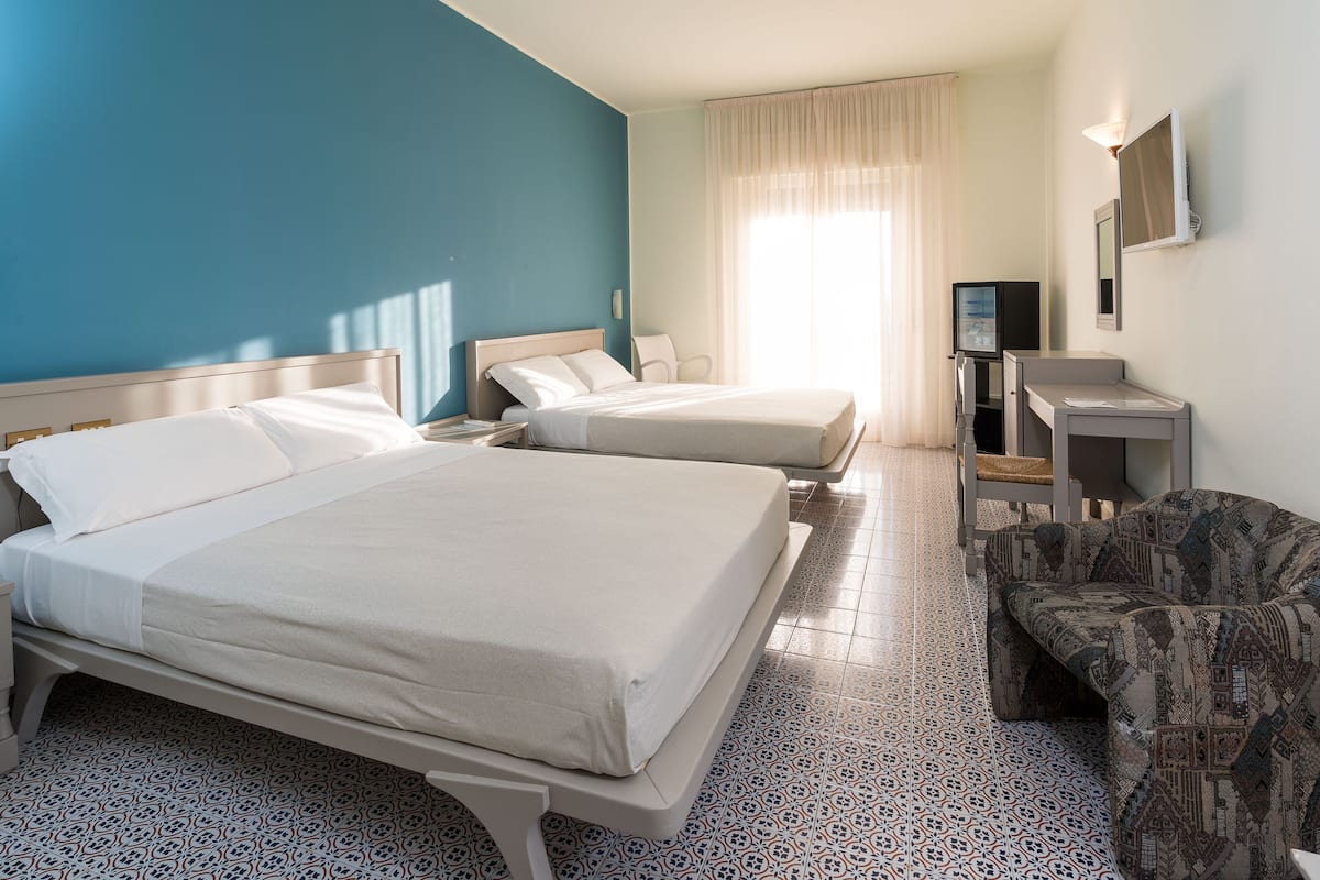 A hotel room with two beds, a TV, a desk, and a patterned chair.