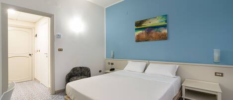 A hotel room with a bed, a chair, a nightstand, a painting on the wall, and a patterned floor.