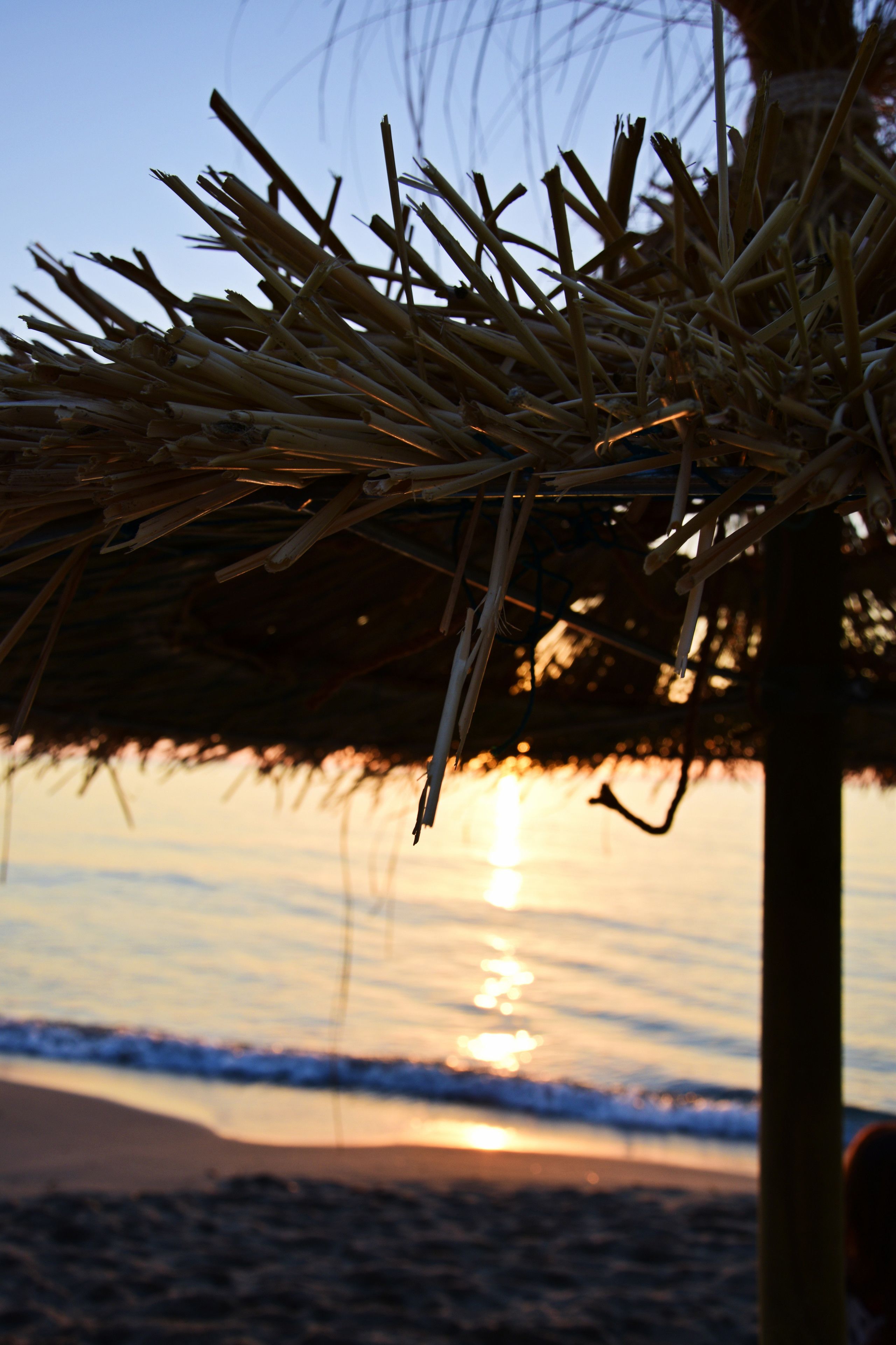 Ein Strandbild mit einer Strohkonstruktion und einem Sonnenuntergang im Hintergrund.
