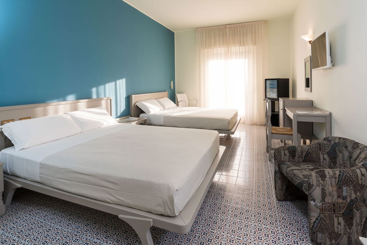 A hotel room with two beds, a desk, a chair, a TV, and a window with curtains.