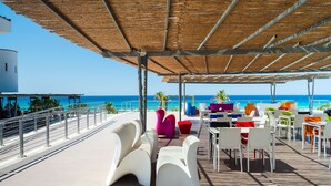An outdoor terrace with white and colorful seating, a view of the ocean, and a wooden deck. - Saracen Sands Hotel & Congress Centre (Isola delle Femmine)