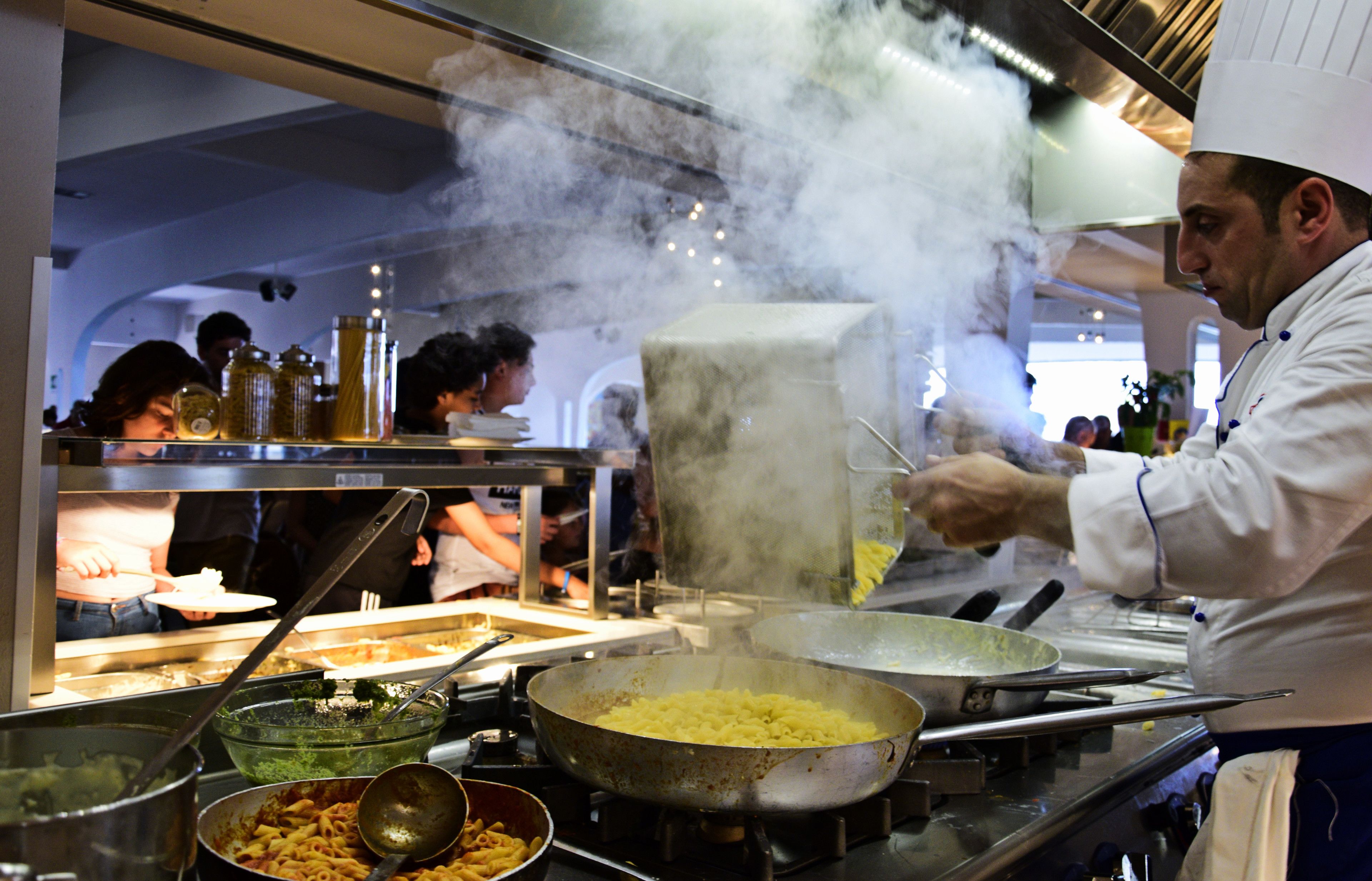 Een kok aan het koken in een professionele keuken, met verschillende keukengerei en ingrediënten in het zicht.