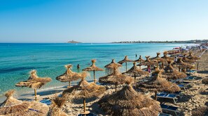 A beach with thatched umbrellas and sun loungers, clear blue water, and a distant island. - Saracen Sands Hotel & Congress Centre (Isola delle Femmine)