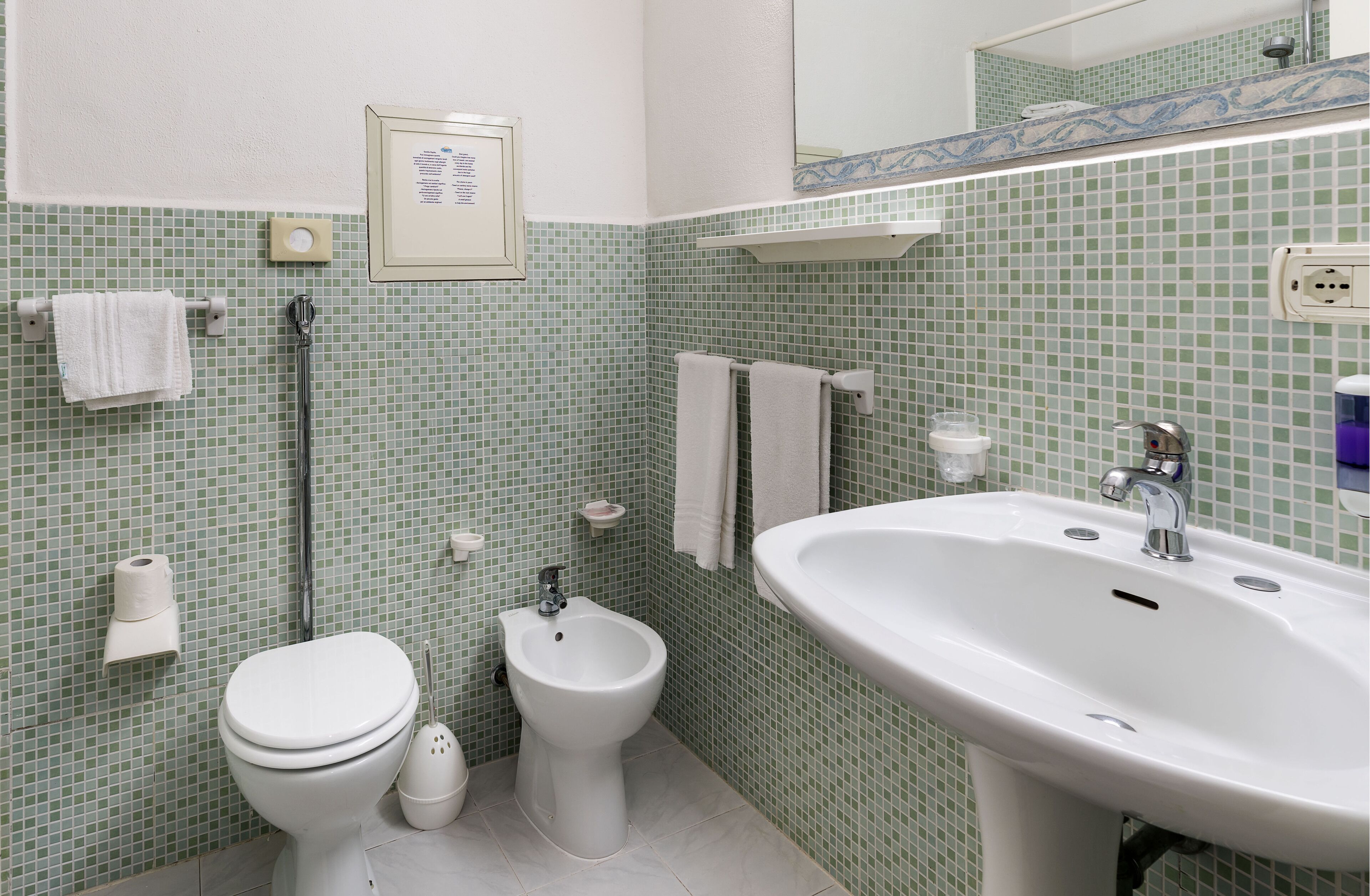 Un bagno con WC, bidet, lavandino e pareti piastrellate.
