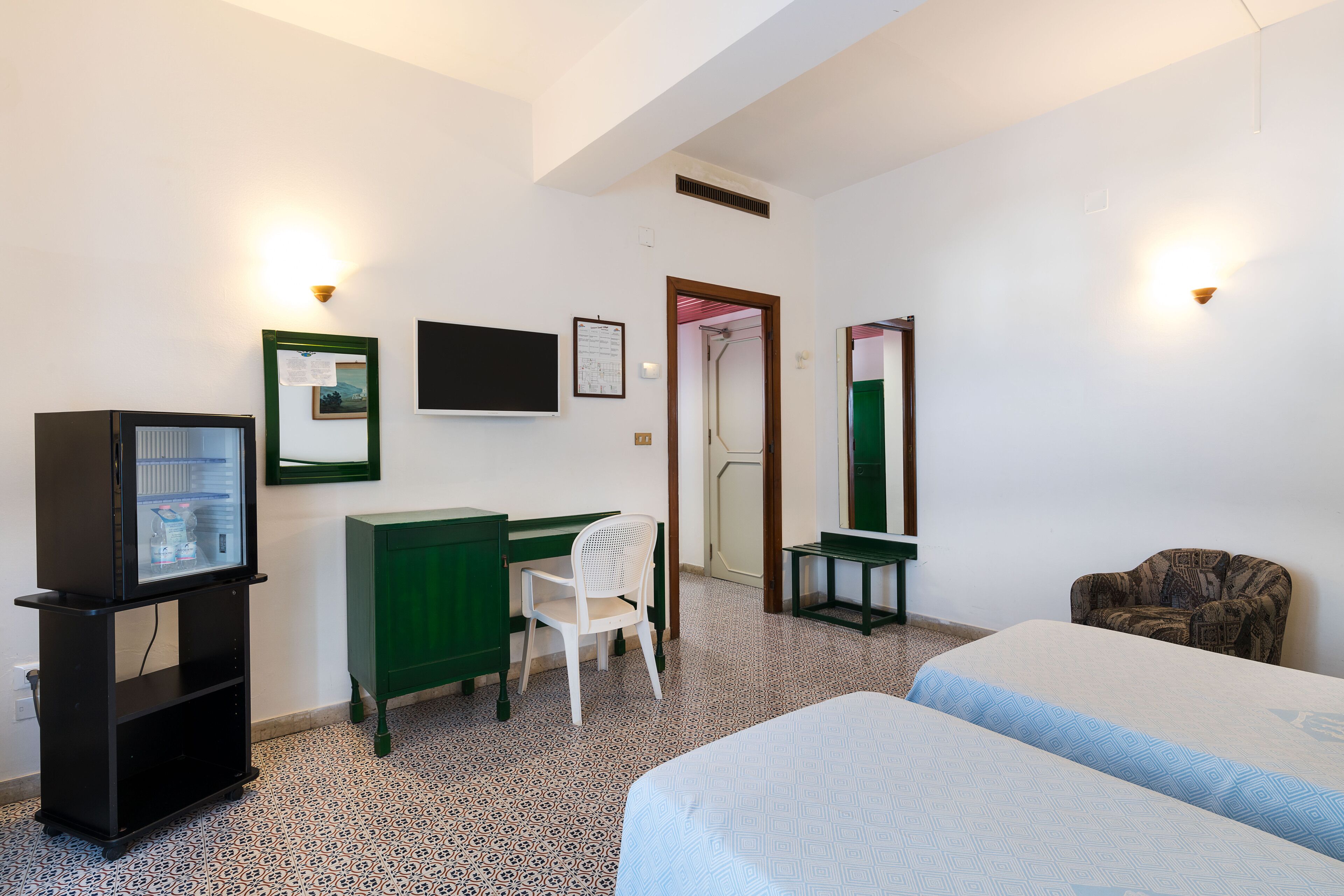 A hotel room with a bed, a desk with a chair, a television, and a mirror.
