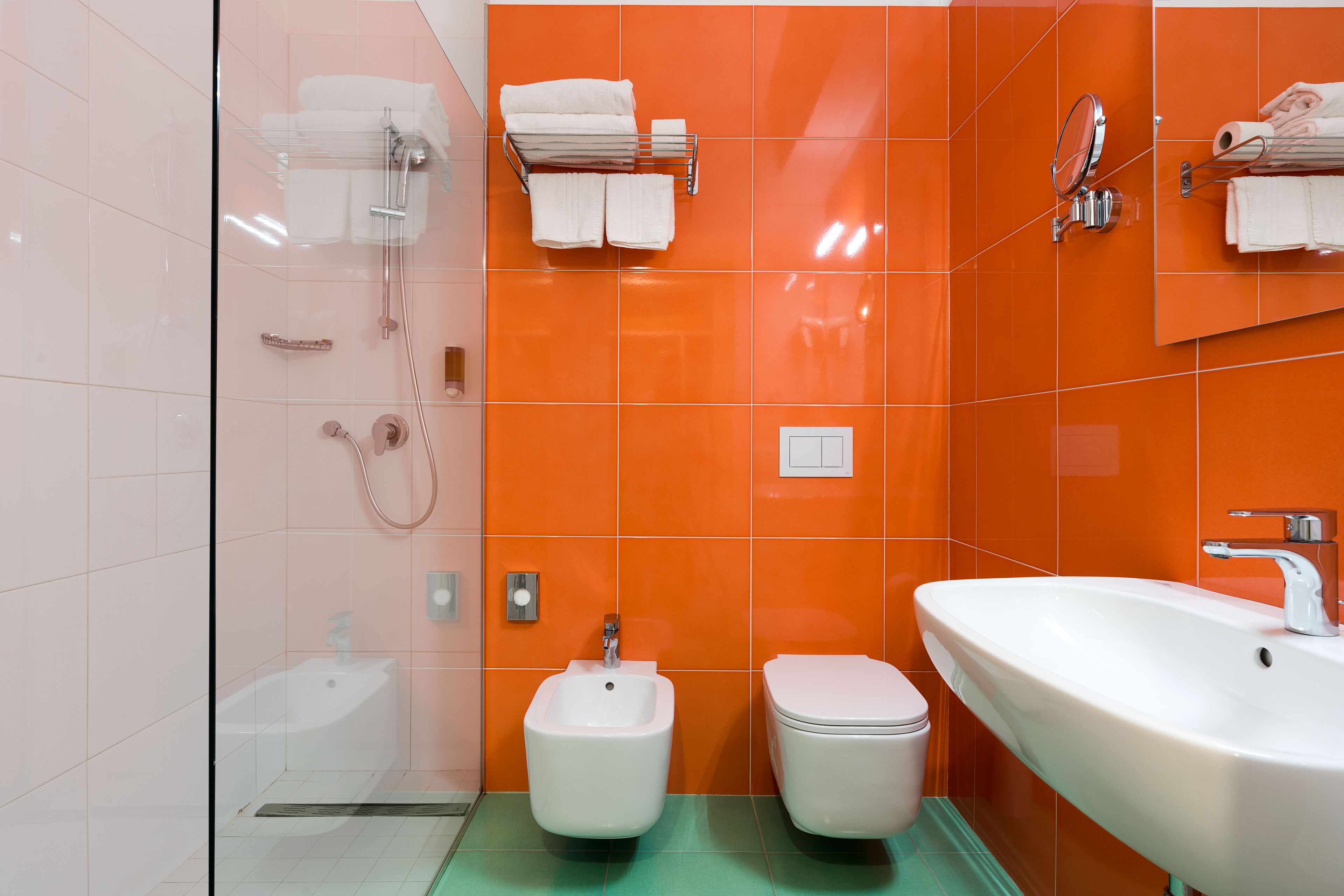 A bathroom with a glass shower enclosure, a bidet, a toilet, and a sink.
