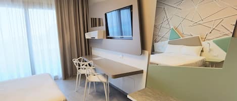 A modern hotel room with a bed, a desk, a chair, a TV, and a geometric wall design.