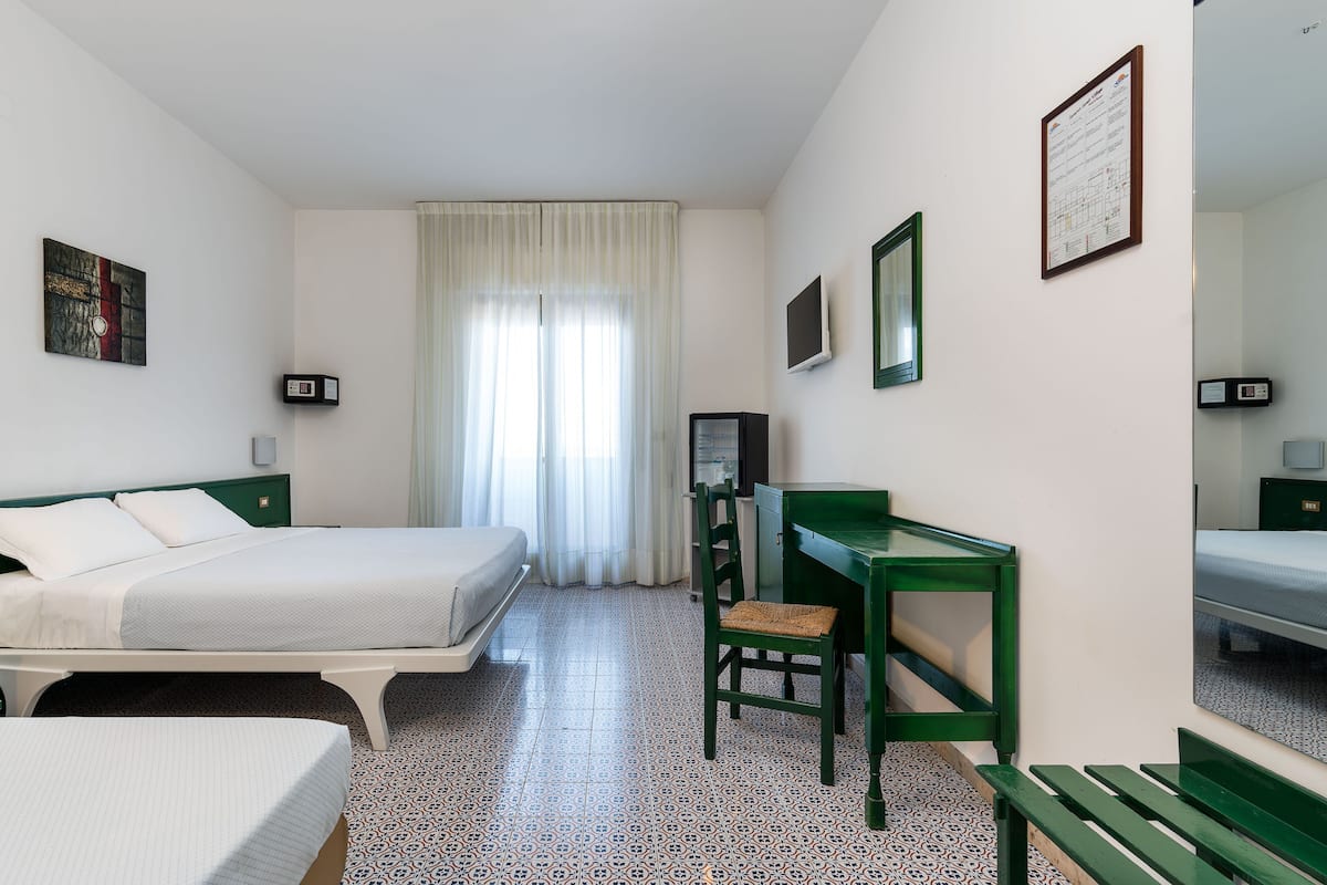 A hotel room with two beds, a desk, a chair, a mirror, and a window with curtains.