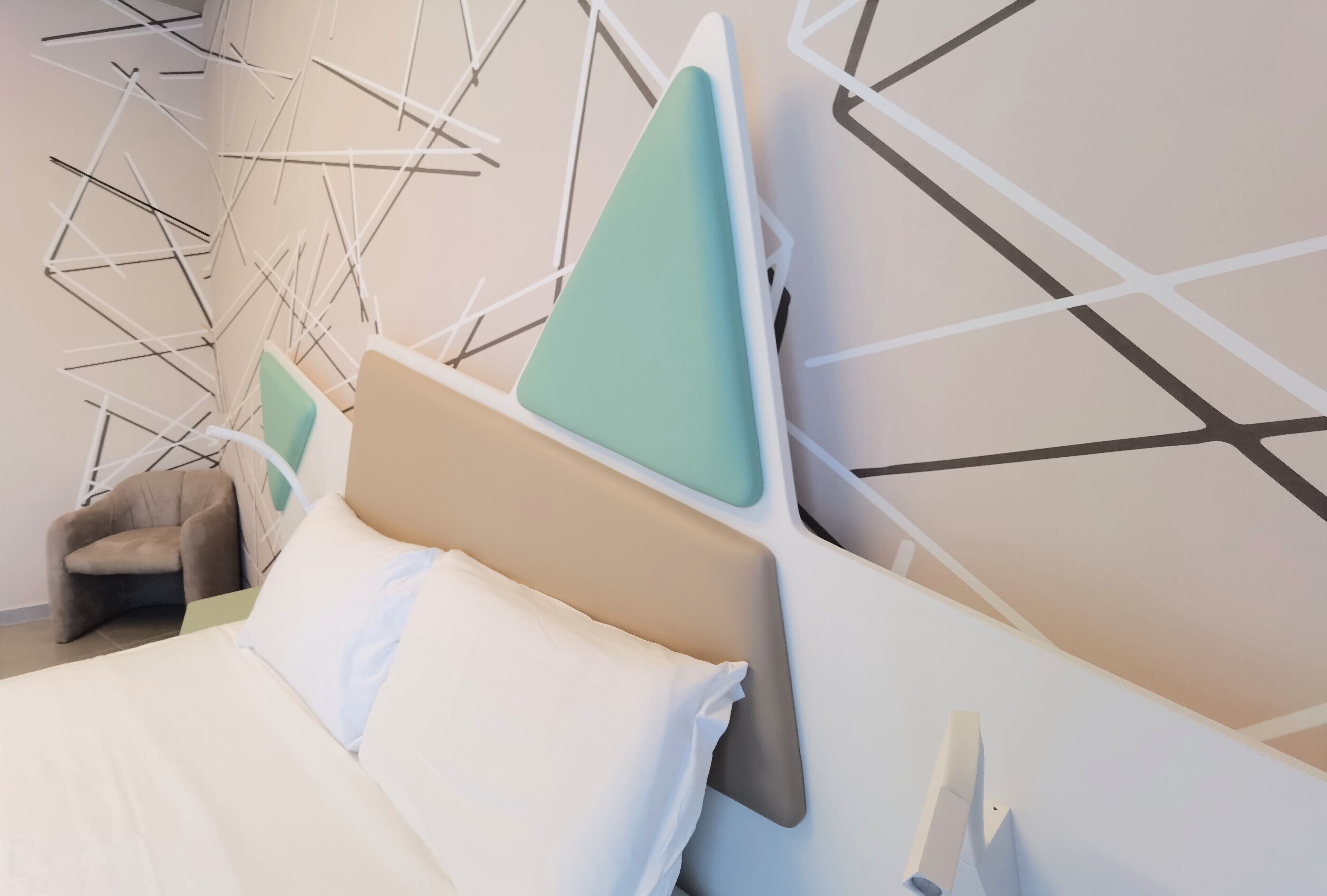 A modern hotel room with a bed, a chair, and a geometric wall design.