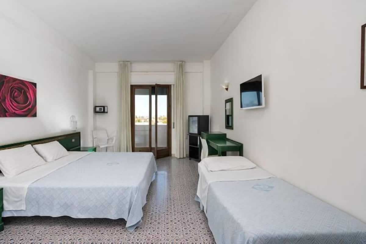 A hotel room with two beds, a TV, a desk, and a window with a view.