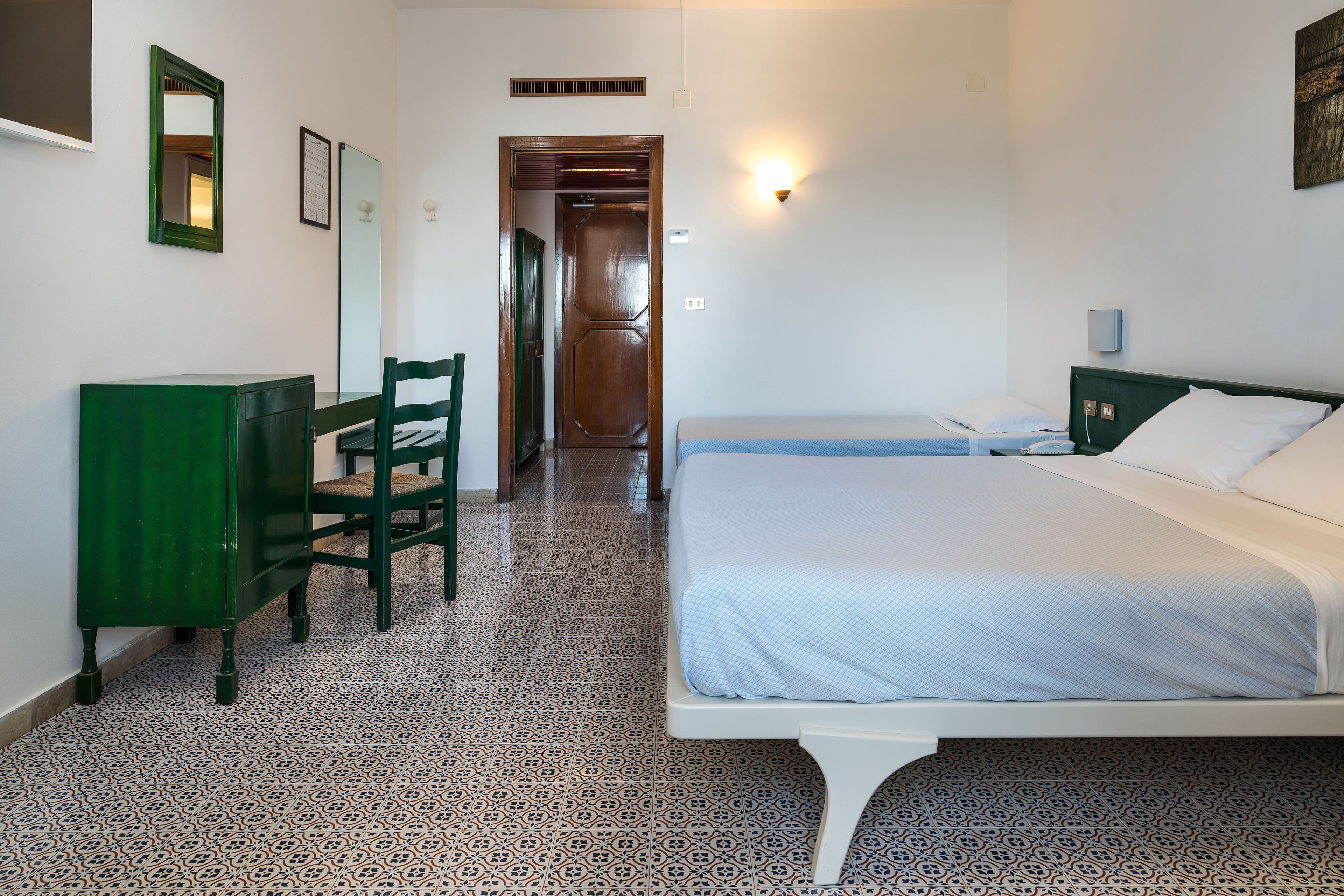 A bedroom with a bed, a desk, a chair, and a mirror.