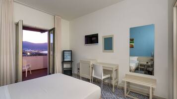 Ein Hotelzimmer mit Bett, Schreibtisch, Stuhl, Fernseher und einem fensterbepflanzten Fenster.