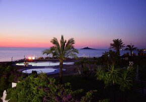 Zona de piscina con palmeras y vista al atardecer.