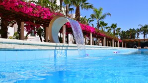 A swimming pool with a water feature, surrounded by palm trees and pink flowers. - Saracen Sands Hotel & Congress Centre (Isola delle Femmine)