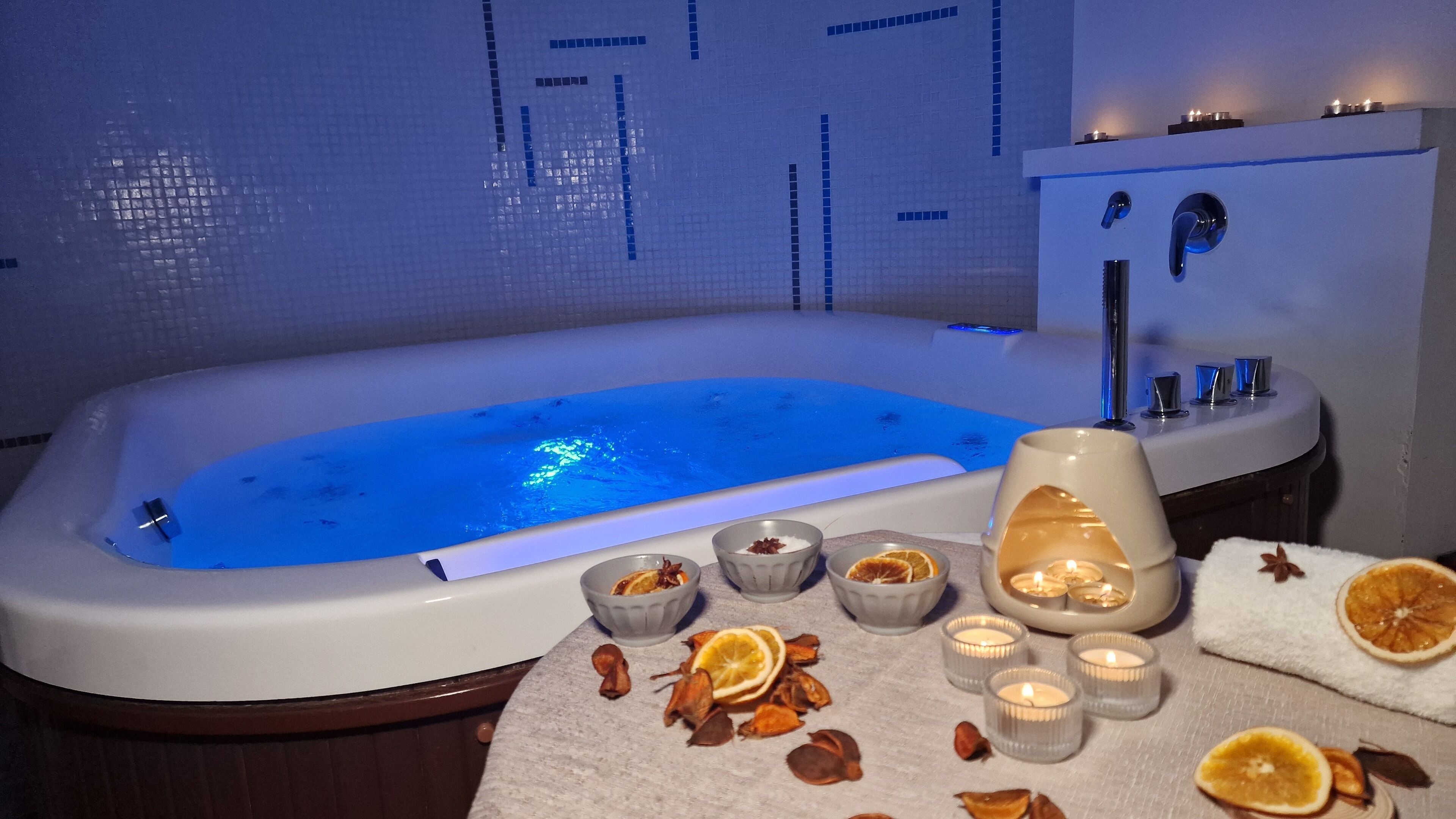 A modern bathroom with a large bathtub, a sink, and a mirror. There are candles and dried orange slices on the counter.