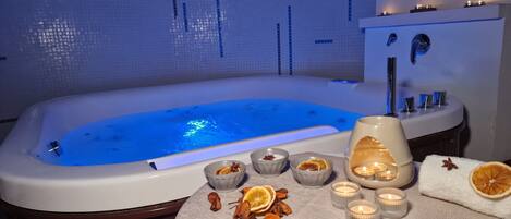 A modern bathroom with a large bathtub, a sink, and a mirror. There are candles and dried orange slices on the counter.