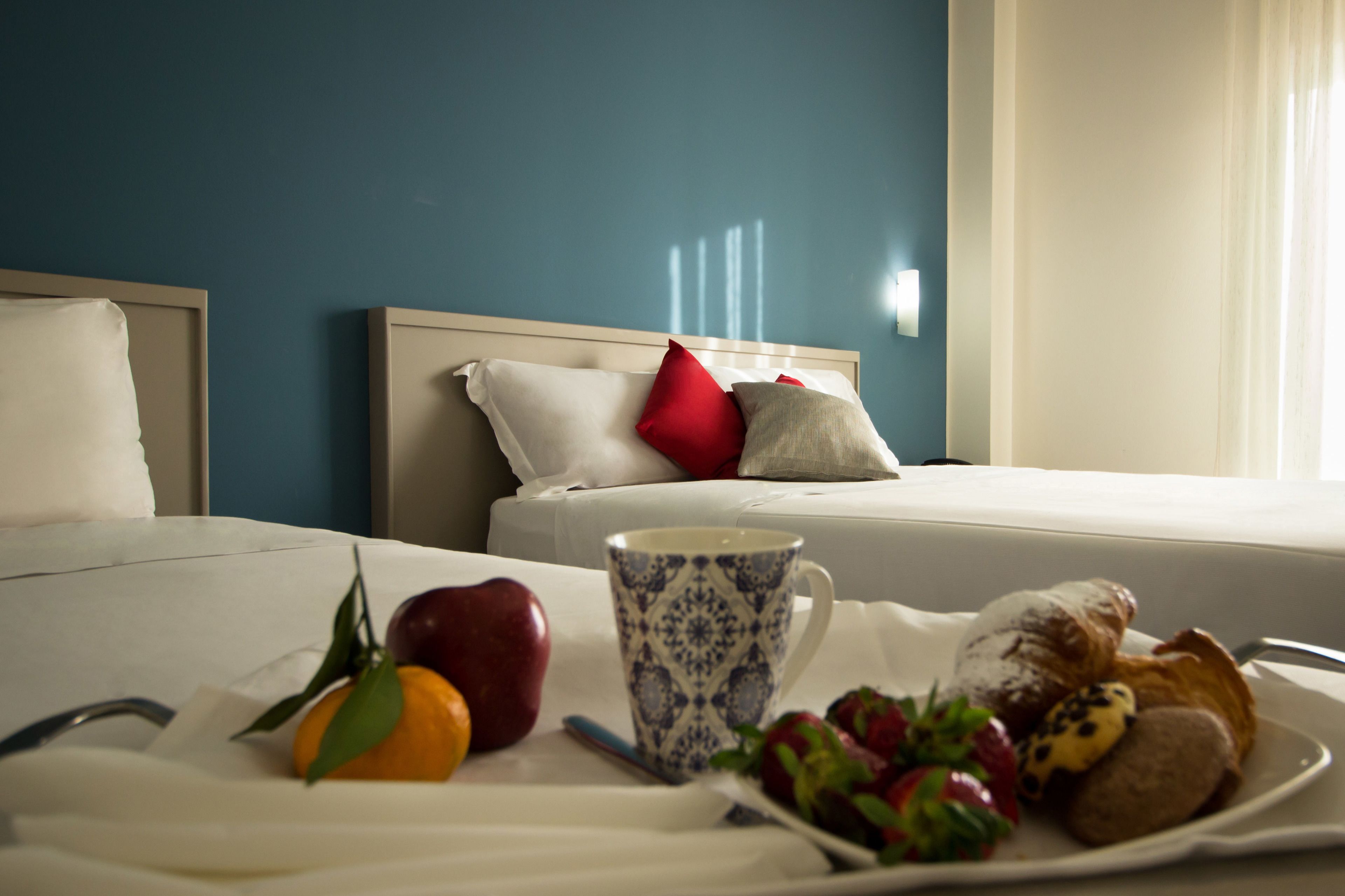 Een hotelkamer met een bed, een nachtkastje met ontbijtartikelen en een raam met gordijnen.