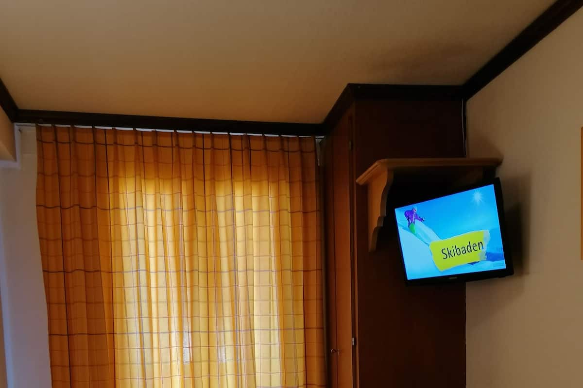 Ein Hotelzimmer mit einem Bett, einem Schreibtisch, einem Fernseher, der 'Skibaden' anzeigt, und einer Lampe.