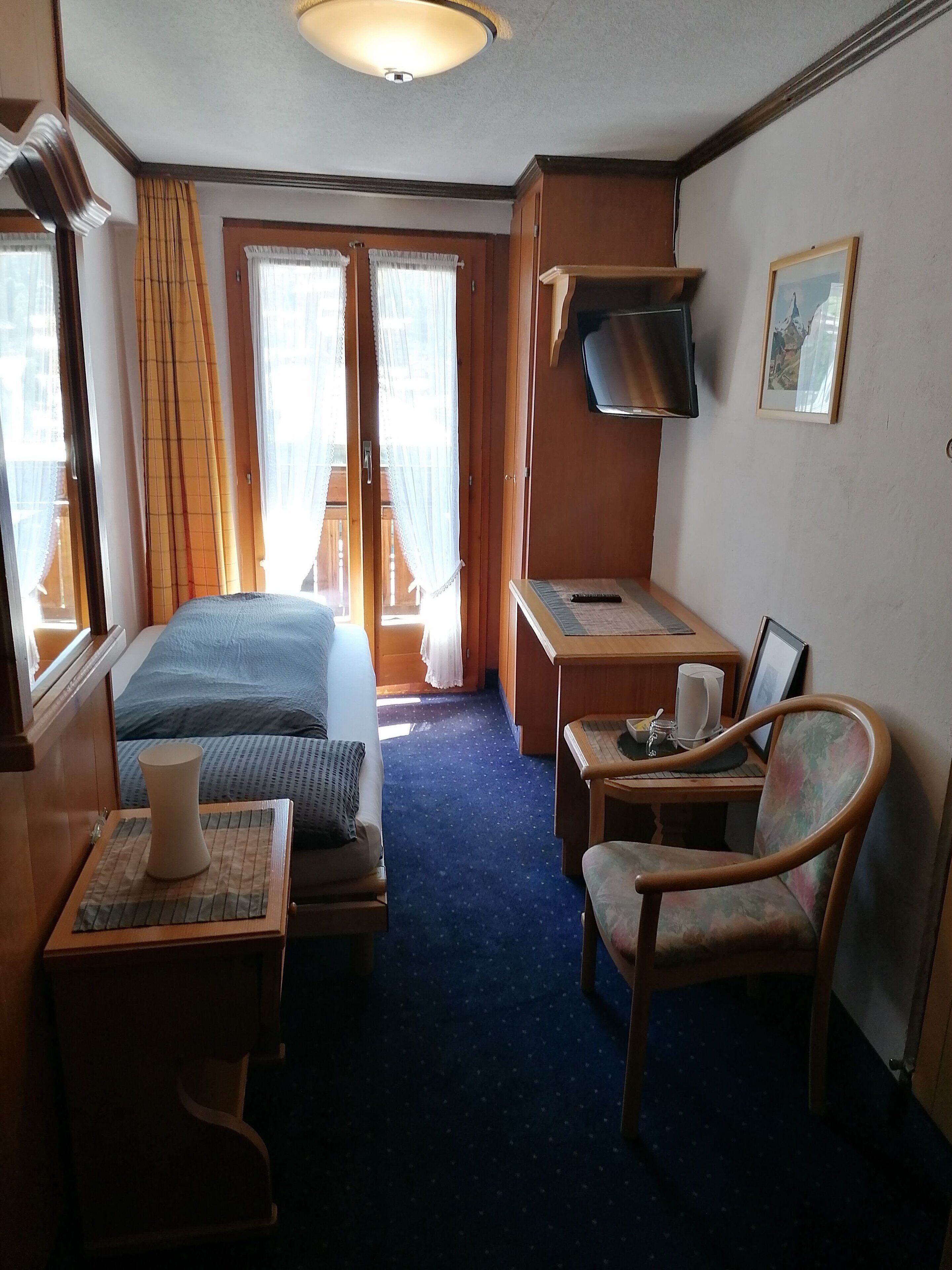 Una habitación de hotel con cama, escritorio, silla, televisor y ventana con cortinas.