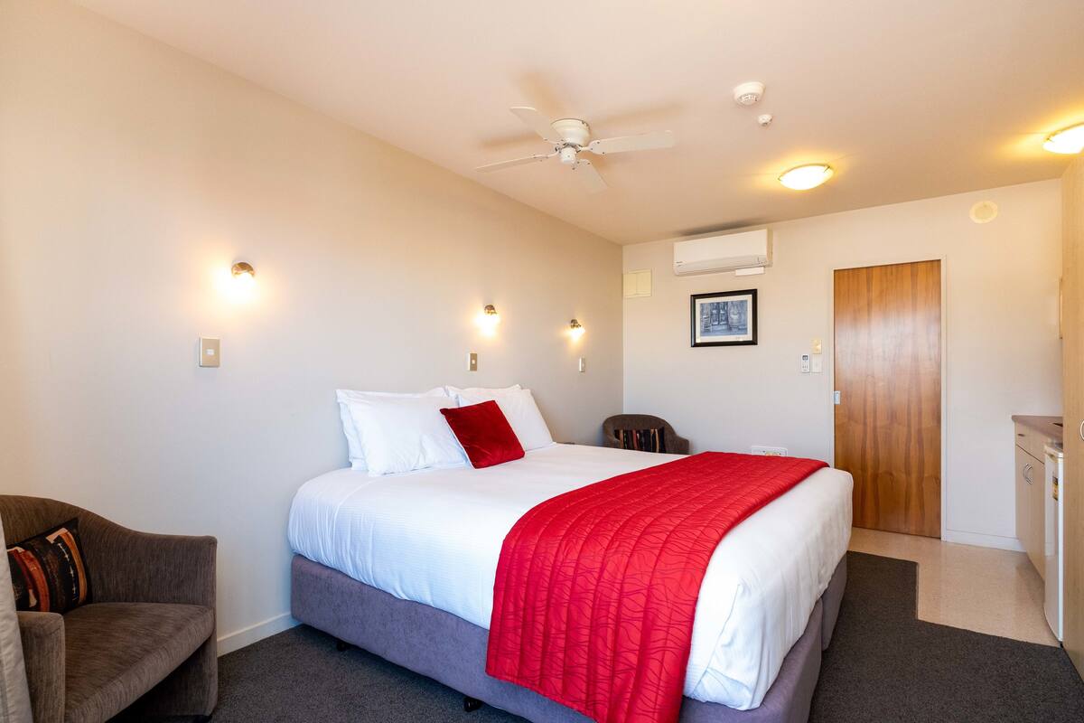 A hotel room with a bed, a desk, a chair, and a ceiling fan.