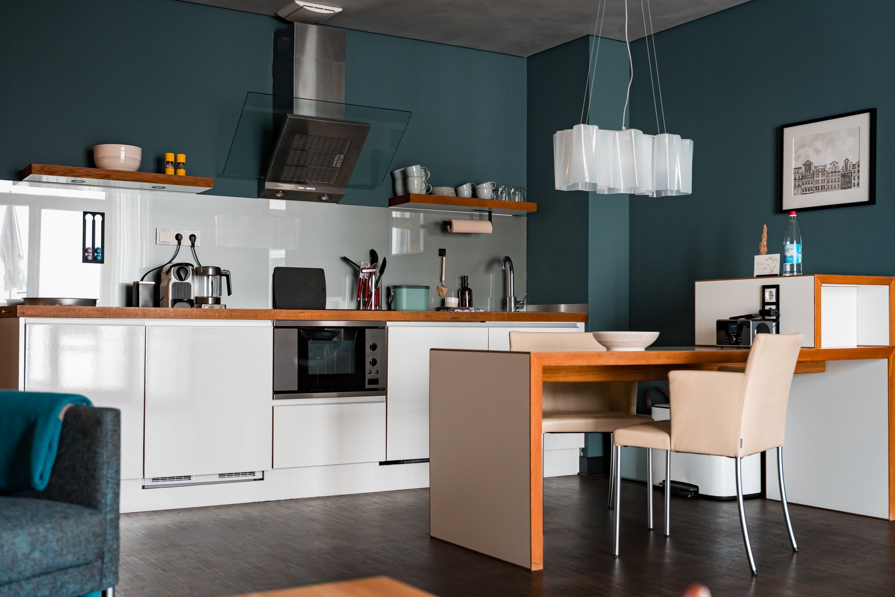A modern kitchen with white cabinetry, a built-in oven, and a dining area with a wooden table and chairs.