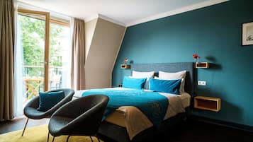 Ein Schlafzimmer mit einem Bett, zwei Stühlen, einem Nachttisch und einem Fenster mit Vorhängen.
