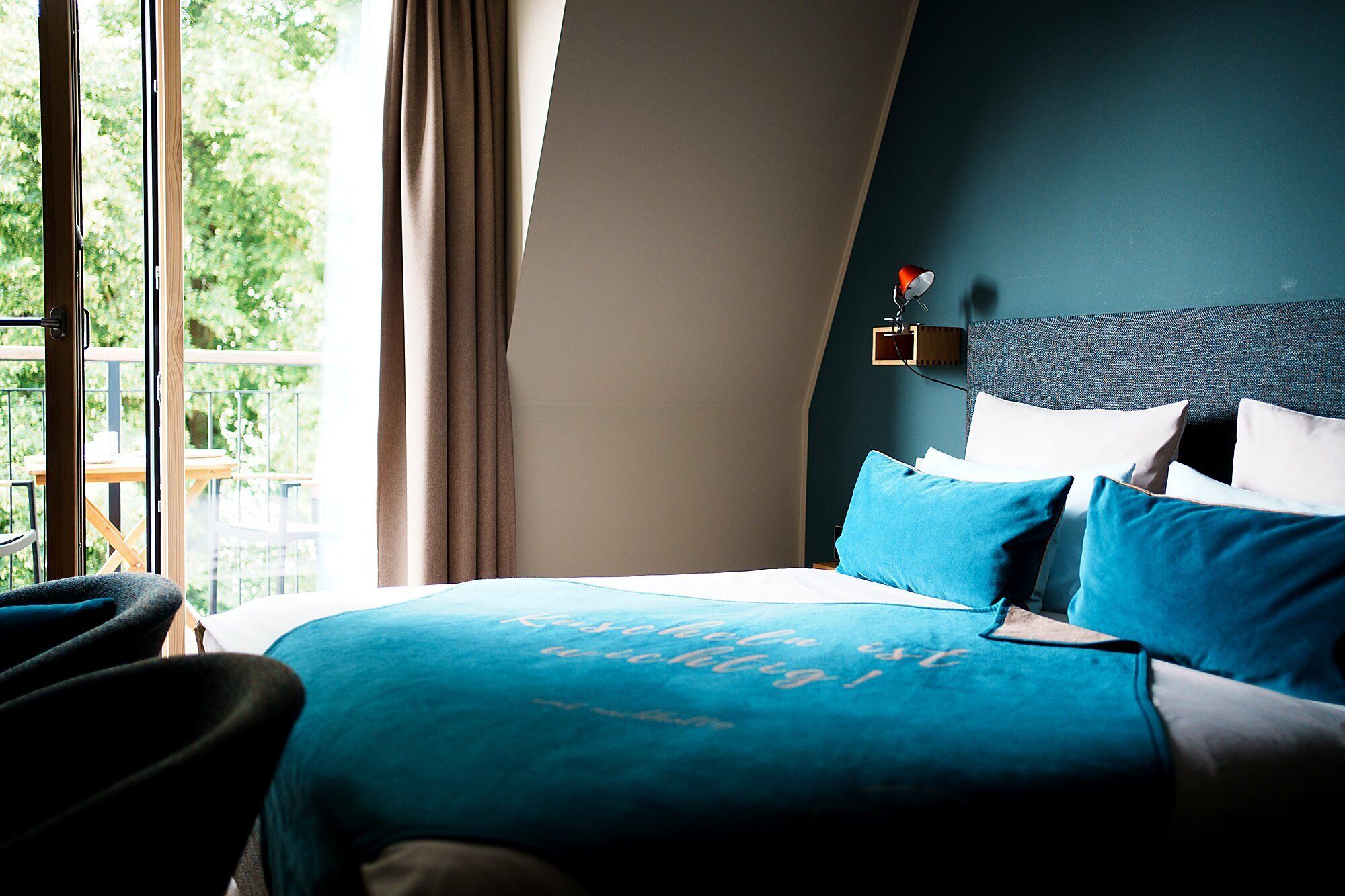Une chambre d’hôtel avec un lit, une table de chevet, une lampe et une vue sur la verdure.
