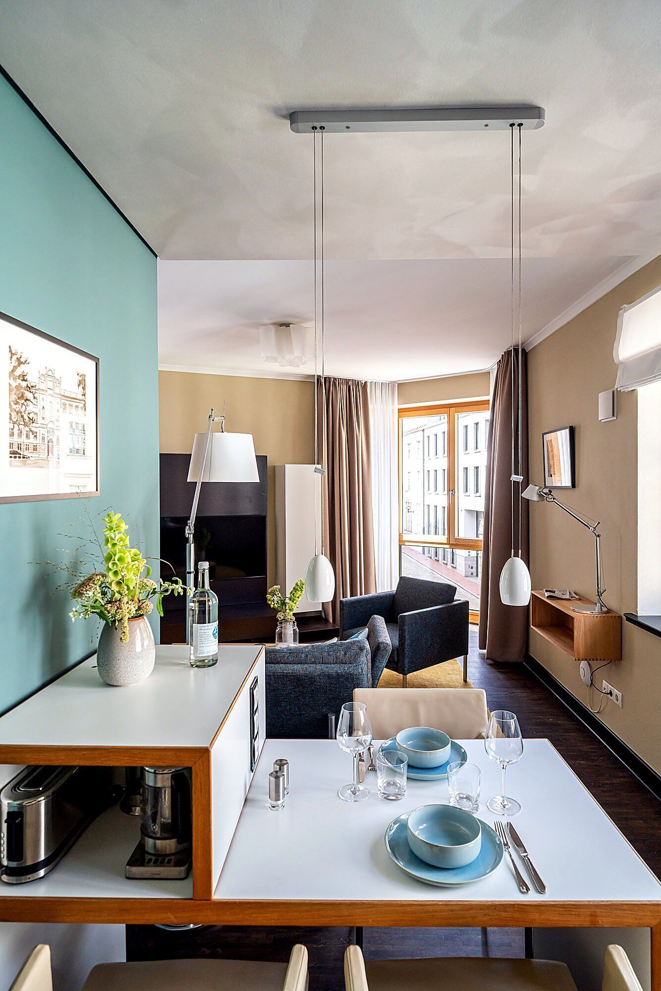 A modern living room with a dining area, featuring a sofa, a coffee table, and a view of the city through large windows.