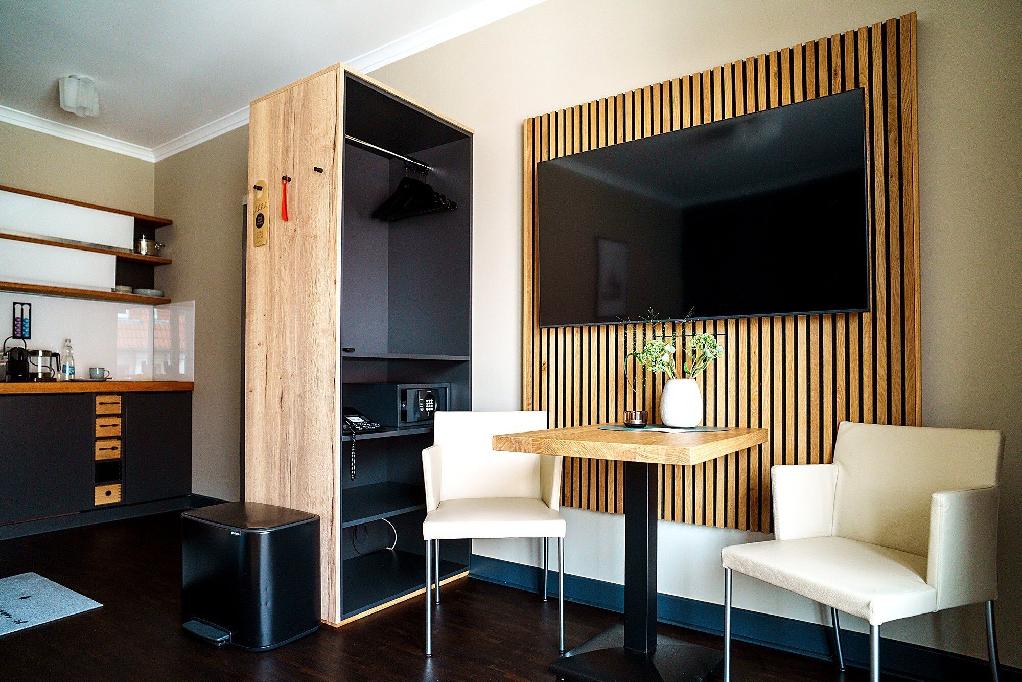 Un espacio habitable moderno con un mueble de madera, un televisor de pantalla plana, una pequeña mesa con sillas y una cafetera.