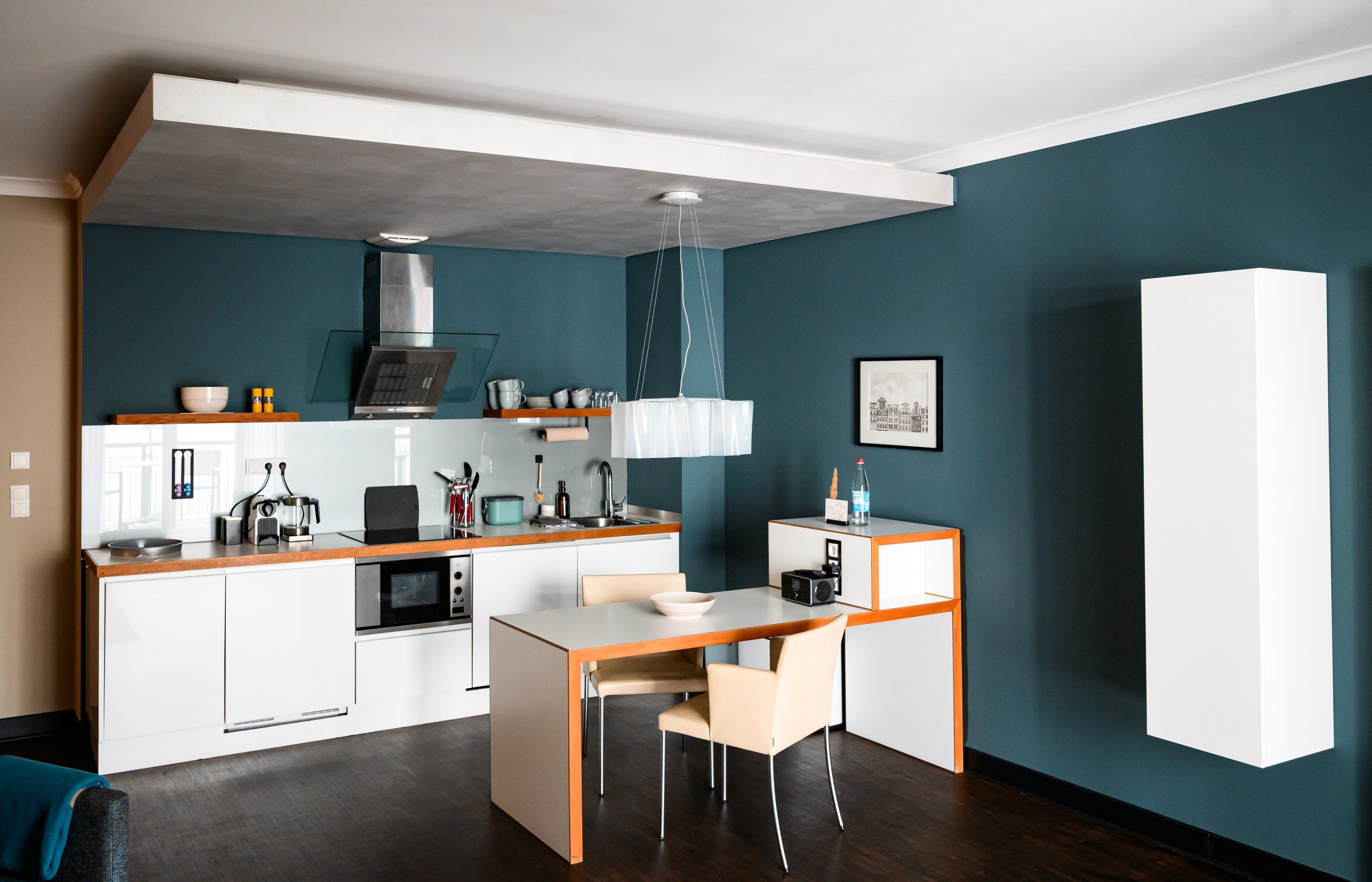 A compact kitchen with a microwave, stove, and modern appliances, a dining area with a table and chairs, and a large white cabinet.