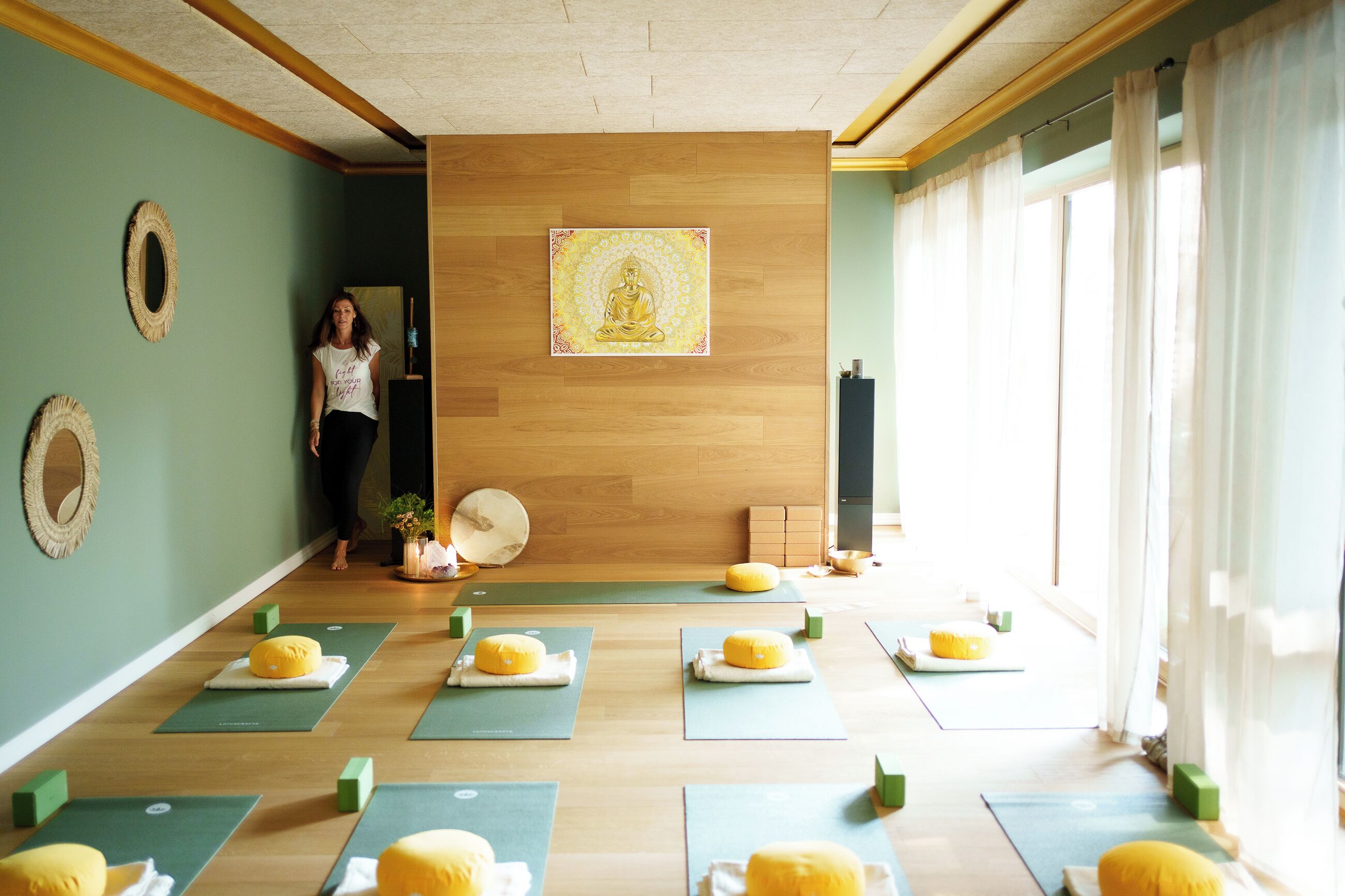 Uno studio di yoga con tappetini, un'area per la meditazione e una grande statua di Buddha sulla parete.