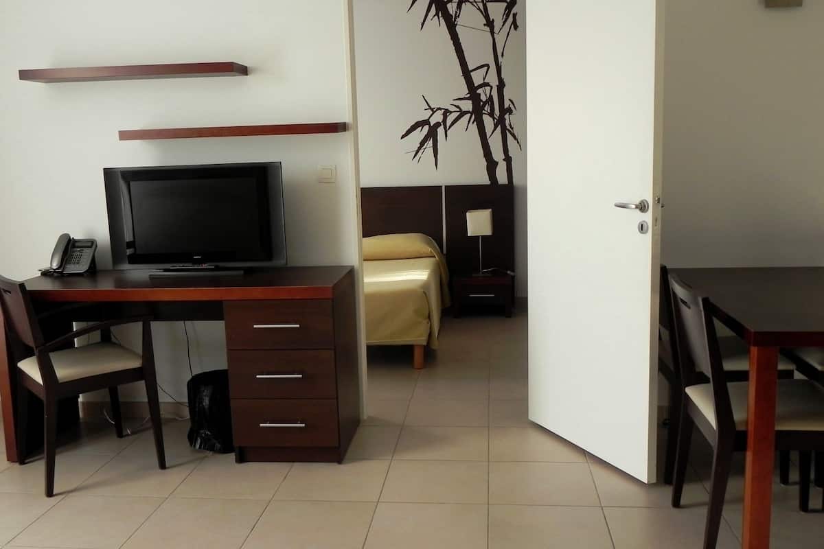 A hotel room with a desk, chair, bed, bedside table, lamp, and a wall with a bamboo decoration.