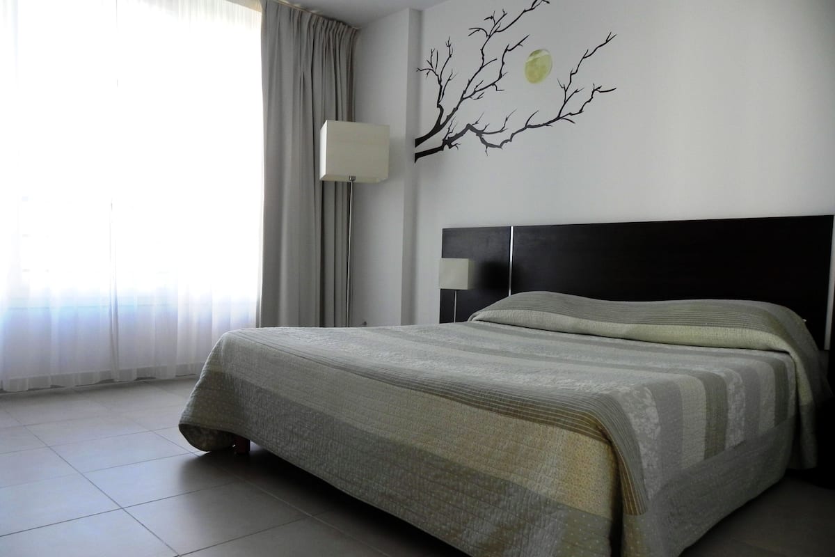 A hotel room with a bed, a nightstand, a lamp, and a wall art piece.