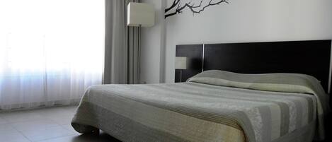 Hotellihuone, jossa on sänky, yöpöytä, lamppu ja seinätaideteos.
