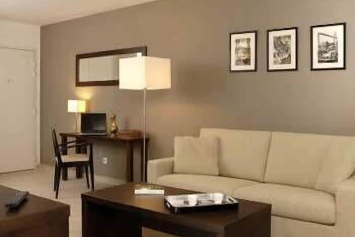 A living room with a sofa, a coffee table, a desk with a lamp, and three framed pictures on the wall.