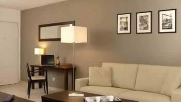 Ein Wohnzimmer mit einer Couch, einem Couchtisch, einem Schreibtisch mit Lampe und drei gerahmten Bildern an der Wand.