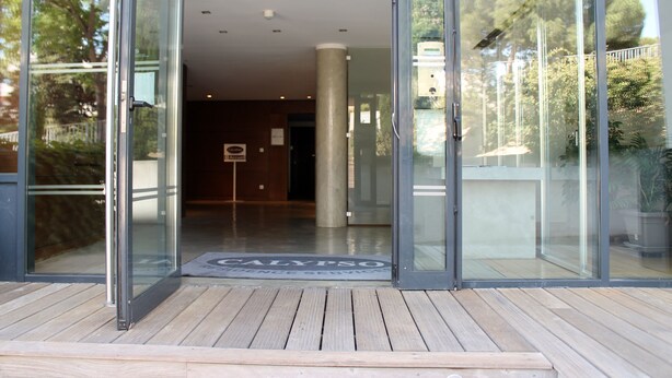 A modern building entrance with glass doors, a wooden deck, and a sign reading "CALYPSO". - Residence Calypso (Marseille)