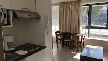Cozinha moderna com fogão embutido, máquina de café e telefone. Possui área de refeições com mesa e cadeiras, e uma janela com cortinas.