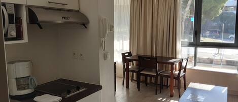 A modern kitchen with a built-in stove, a coffee maker, and a telephone. There is a dining area with a table and chairs, and a window with curtains.