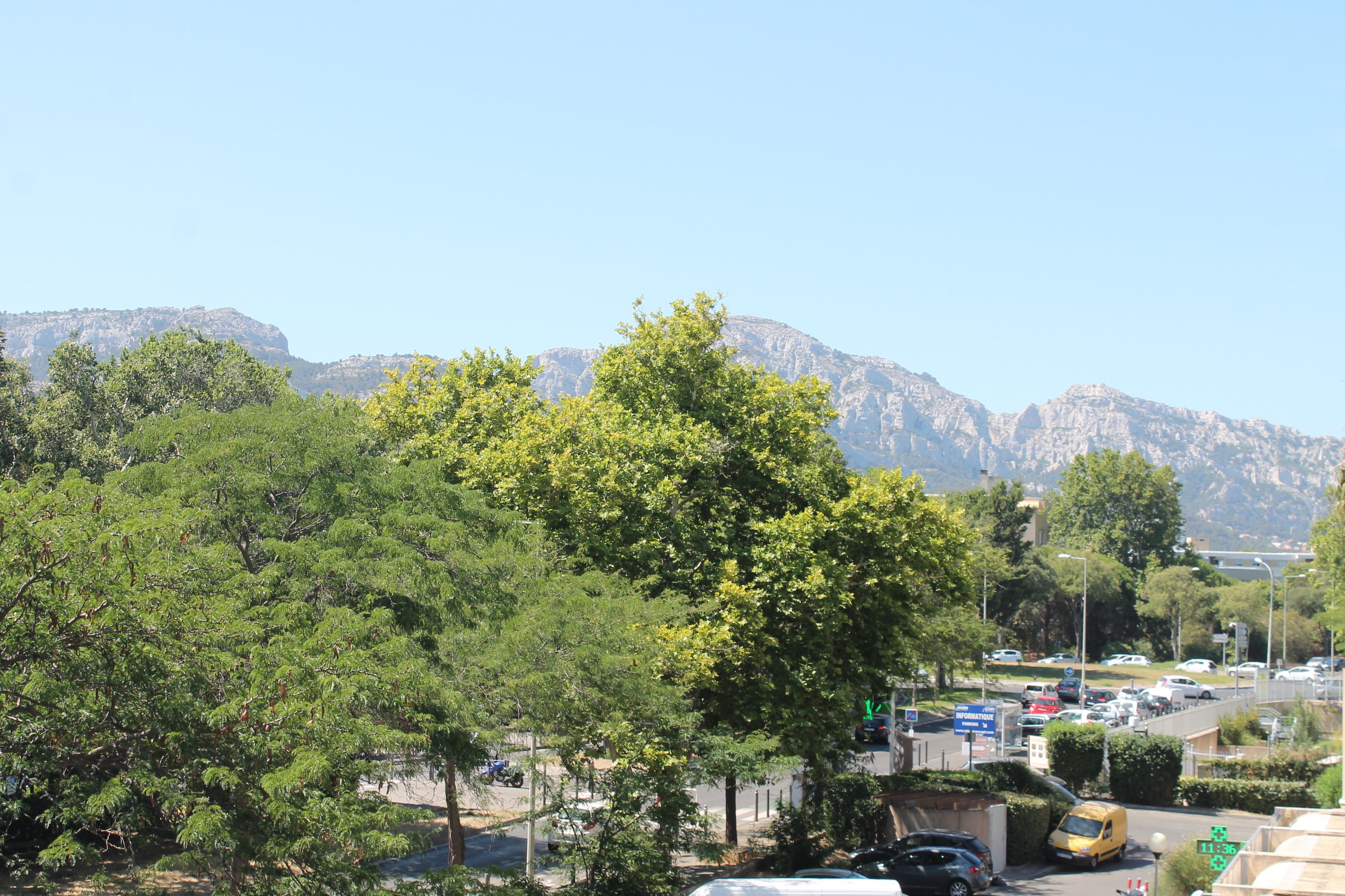 A parking lot with cars and a yellow van, surrounded by trees and mountains in the background.