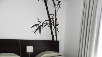 A hotel room with two single beds, a dark headboard, a wall-mounted lamp, and a large black tree decal.